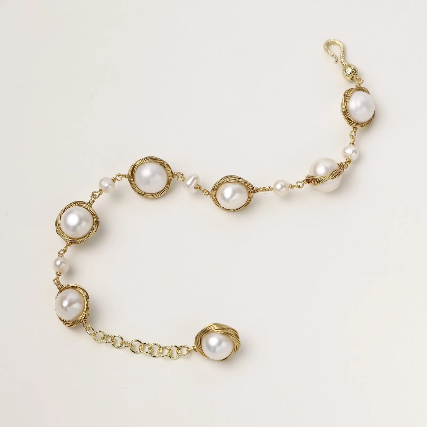 Gold wire-wrapped freshwater pearl bracelet with alternating pearl sizes on cream background, adjustable length