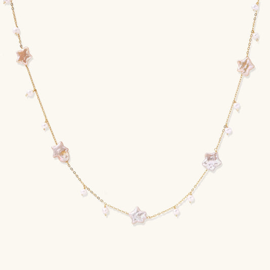 Gold vermeil chain with iridescent star-shaped baroque pearls and small round freshwater pearl drops on cream background.