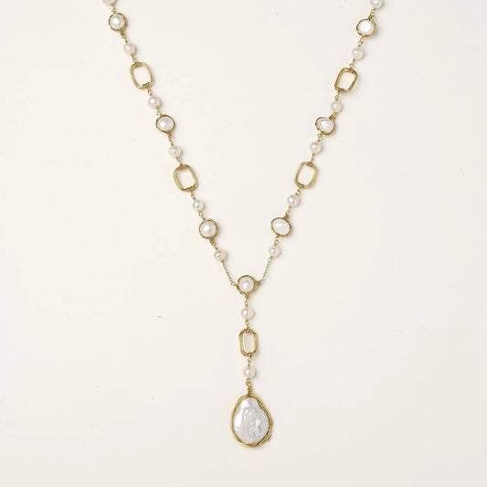 Y-shaped gold necklace with alternating geometric links, freshwater pearls, and baroque pearl pendant on cream background