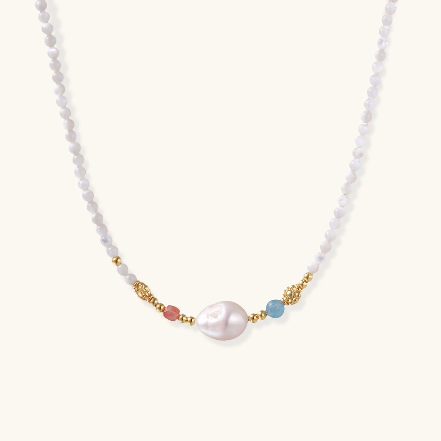Delicate white beaded necklace with baroque pearl center, gold accents, and coral and aqua gemstones on cream background.