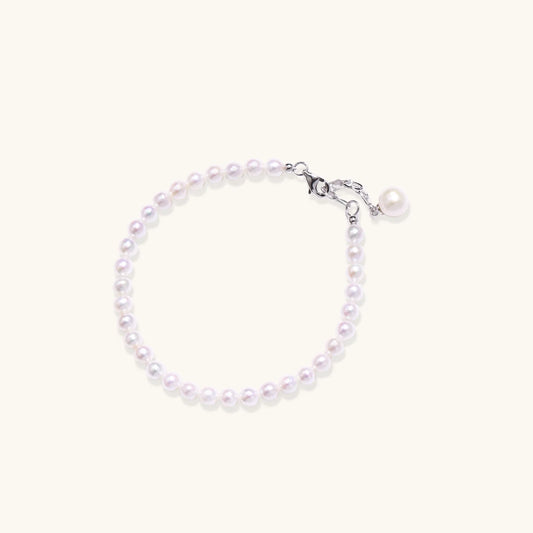 Delicate freshwater pearl bracelet with rhodium-plated silver clasp and single pearl drop charm on cream background