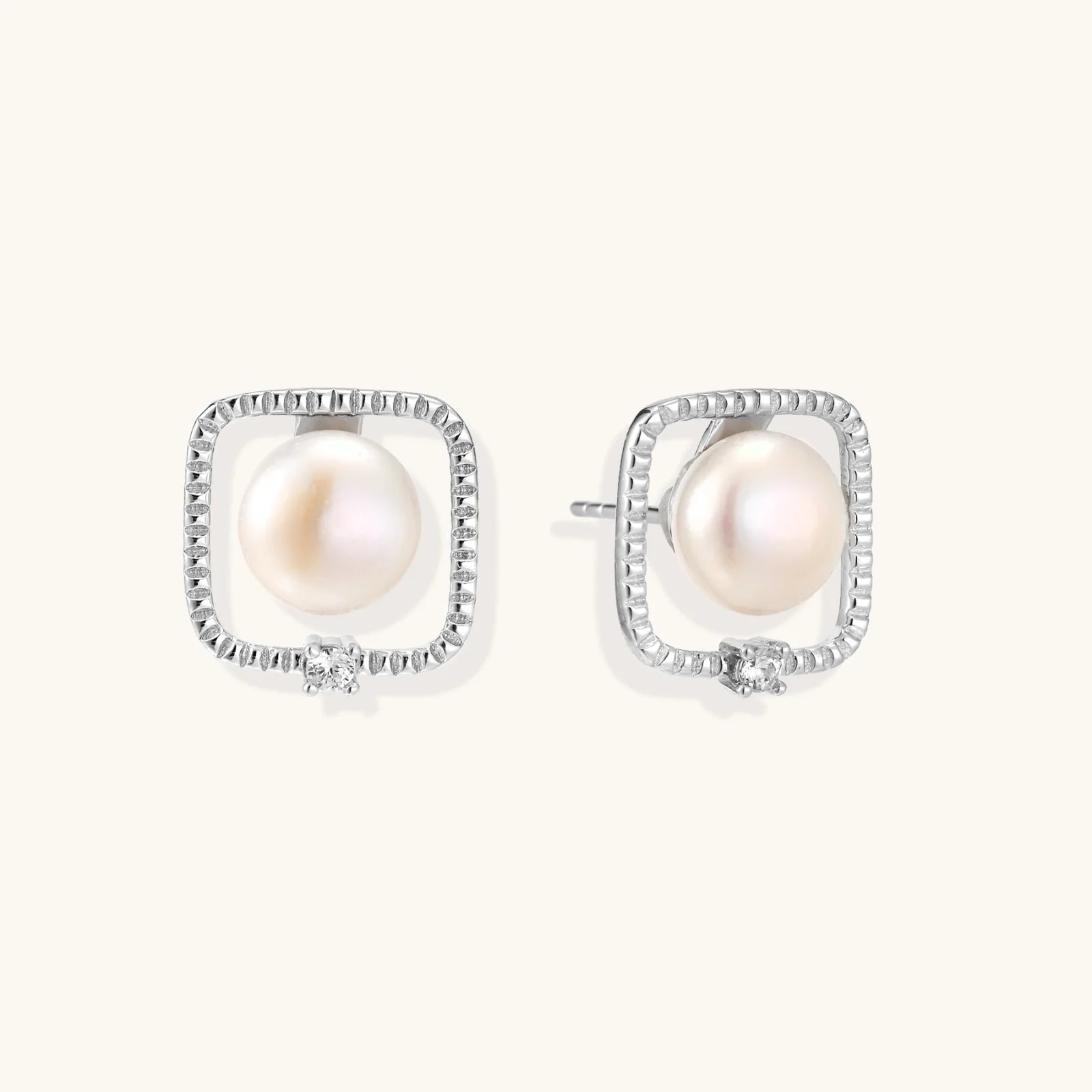 Rhodium-plated silver stud earrings with cushion frame, centered freshwater pearl, and tiny crystal accent