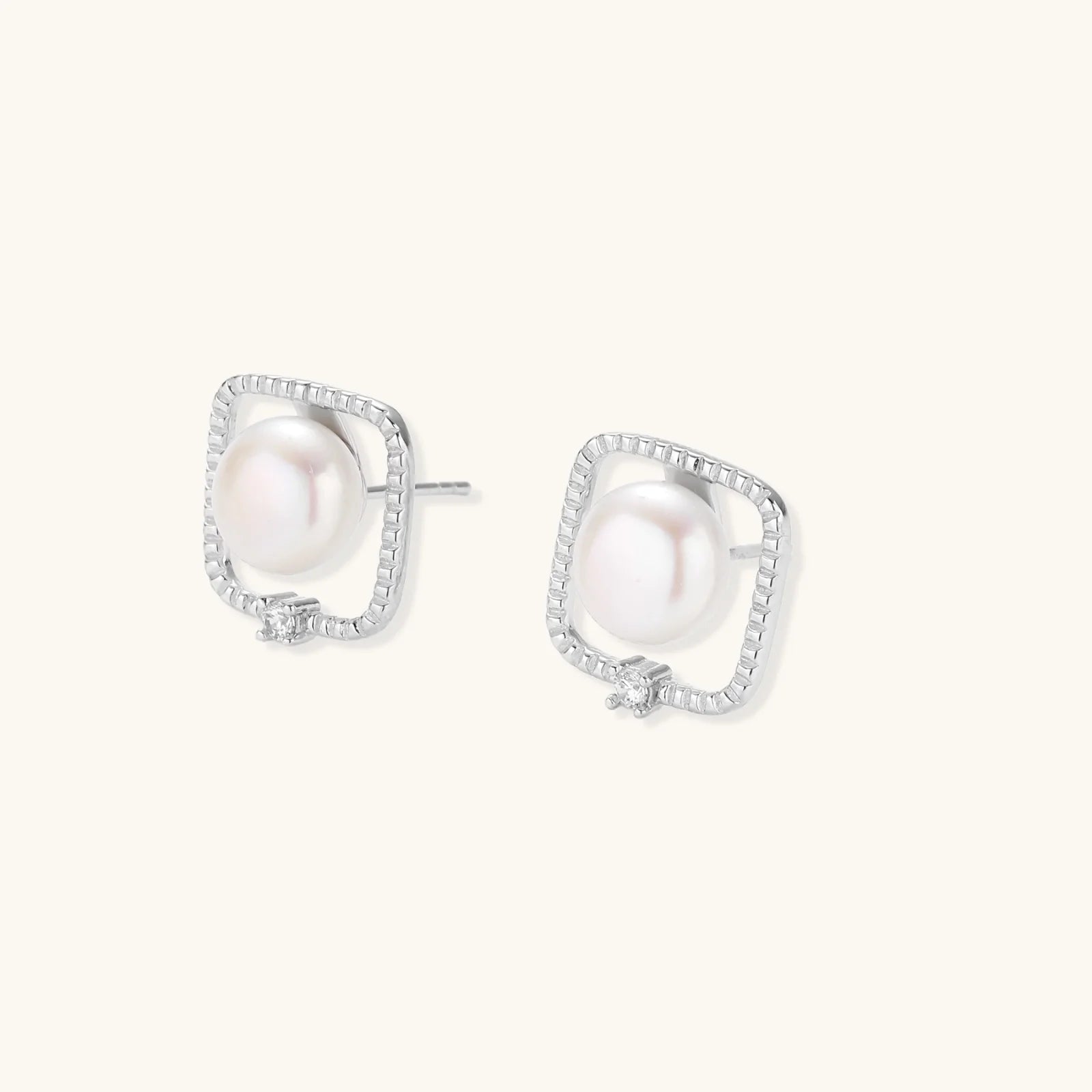 Rhodium-plated silver stud earrings with cushion frame, centered freshwater pearl, and tiny crystal accent