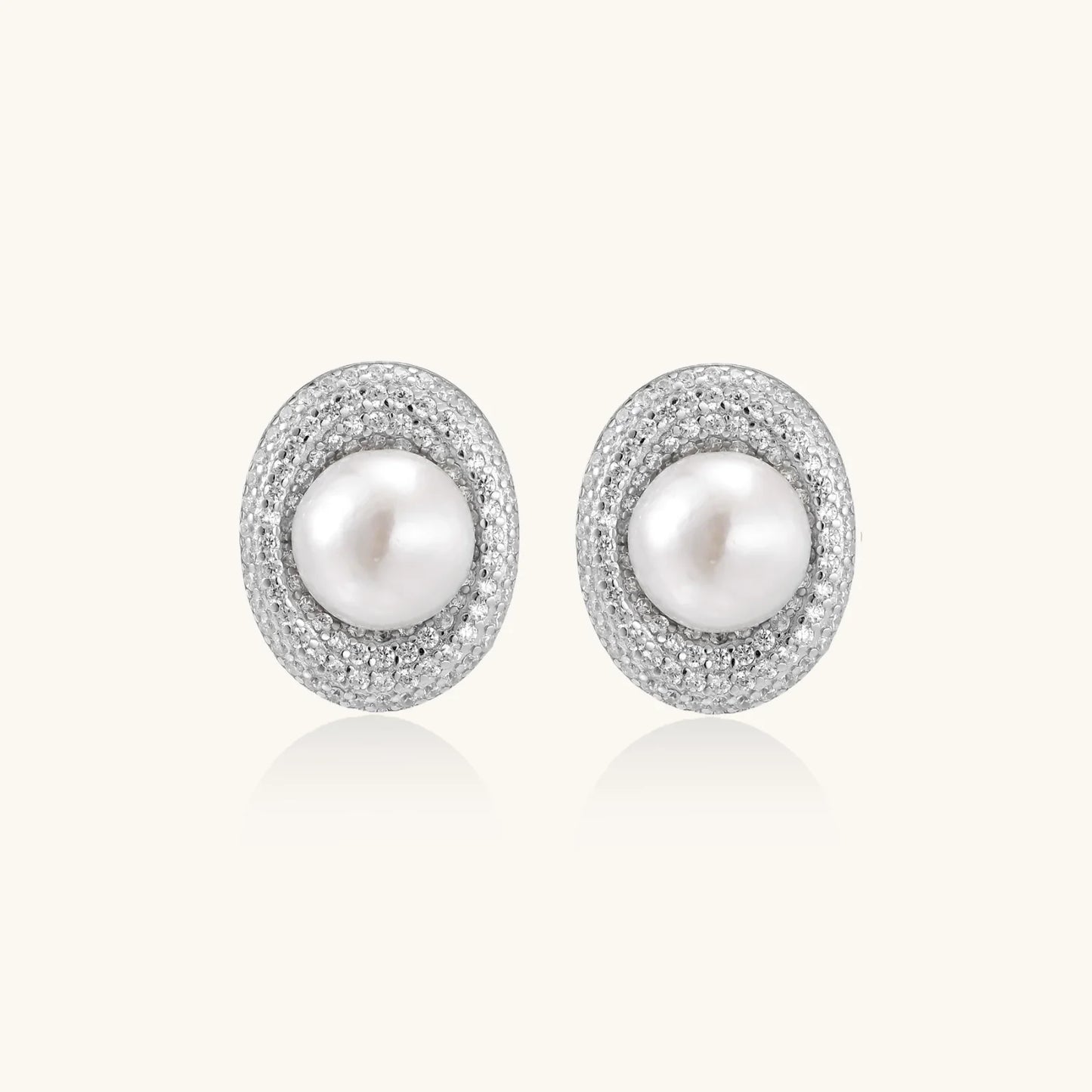 Oval rhodium-plated silver studs featuring freshwater pearls surrounded by pavé crystal halo on white background