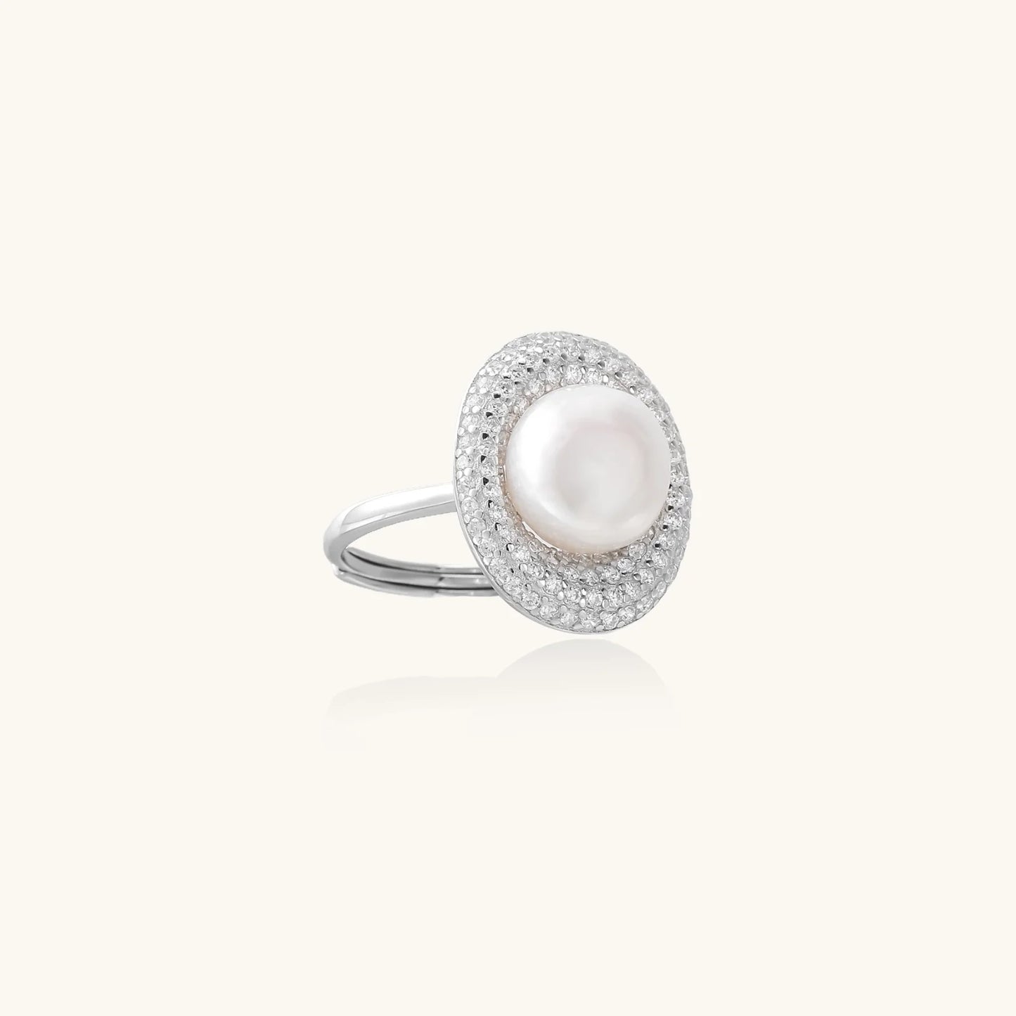 Silver ring with lustrous white pearl center surrounded by sparkling crystal halo on light background.