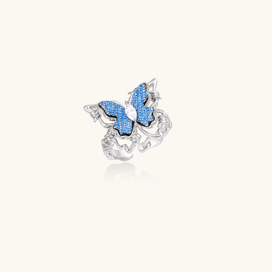 Silver-toned ring with blue denim butterfly wings, marquise zirconia center, and ornate scrollwork band on white background