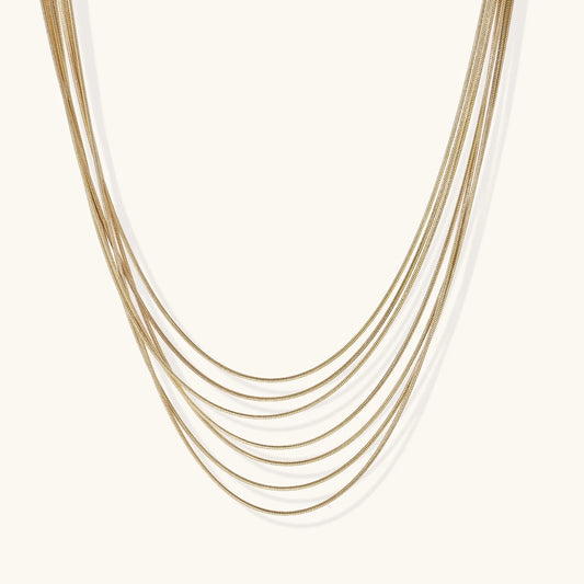 Seven delicate gold-plated snake chains create an elegant layered necklace on a neutral background.