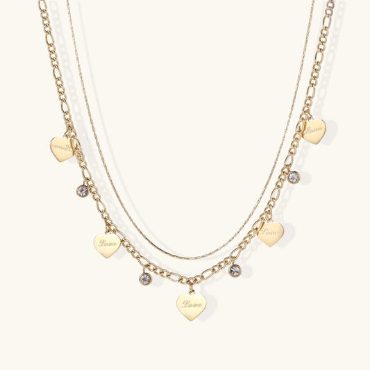 Gold layered necklace set with engraved heart pendants and crystal accents on cream background