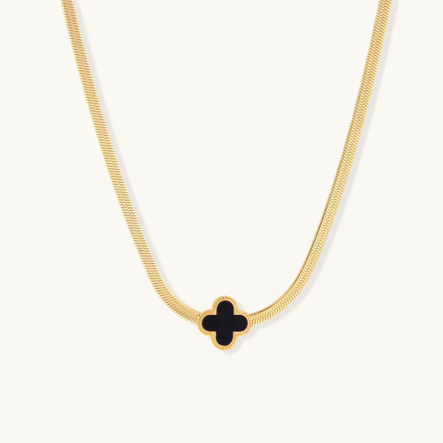 Dainty 18K gold-plated herringbone chain necklace with black enamel quatrefoil clover pendant on white background