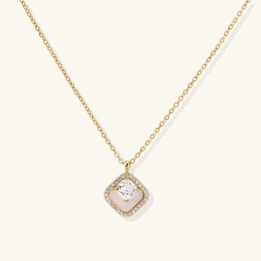 Gold quatrefoil pendant with crystal center on iridescent mother-of-pearl base, adjustable gold chain on cream background